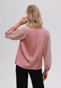 Blusa di satin rosa con maniche lunghe, leggermente a sbuffo, scollo rotondo e vestibilità morbida. Presenta pannelli colorati a contrasto e una texture liscia.