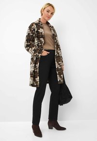 Cappotto in misto lana con un motivo a zigzag nei colori marrone, crema e nero. Abbinato a un maglione marrone, pantaloni neri e stivali con tacco marrone scuro.