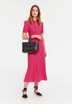 Robe rose à motifs avec des manches courtes bouffantes, un col à nouer et un ourlet évasé. Sac à main en cuir noir avec des poignées courtes. Chaussures espadrilles.