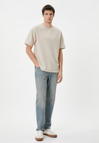 Beige kortærmet, tekstureret t-shirt sat sammen med lyseblå lige ben jeans. Hvide sneakers med brune såler fuldender outfittet.