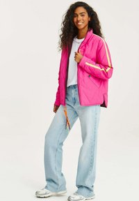 Světle růžová prošívaná bunda s žlutými pruhy, zipem vpředu a nastavovacím táhlem zipu. V kombinaci s světle modrými džíny a stříbrnými teniskami.
