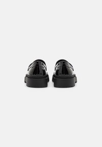 Schwarze Lackleder-Schuhe mit einer massiven Sohle, einem glatten Finish, einer abgerundeten Spitze und einem nahtlosen Design, von hinten betrachtet.