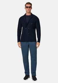 Marineblaues zweireihiges Sakko mit gerippter Textur, kombiniert mit dunkelblauen Hosen. Verfügt über Seitentaschen und wird mit schwarzen Sportschuhen getragen.