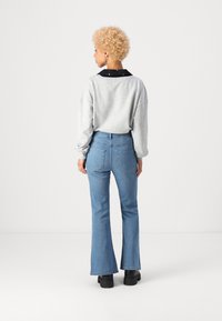 Sweatshirt gris avec col noir, jeans évasés bleus et chaussures à plateforme noires. Vue arrière mettant en valeur les détails de couture et de poches.
