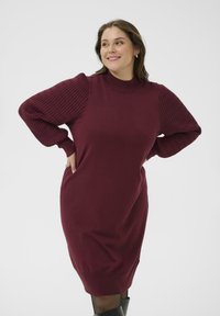 Weinrot Strickkleid mit gerippten, puffartigen Ärmeln; weicher Strickstoff; hoher Kragen; figurbetonter Oberkörper, der zu einem lockeren Saum verläuft.