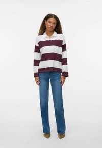 Polo met lange mouwen in bordeauxrood en witte horizontale strepen. Bevat een kraag en een knoopsluiting. Gecombineerd met rechte blauwe jeans.