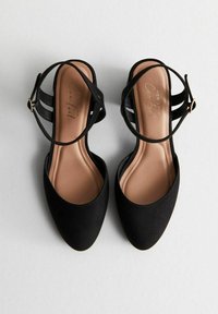 Scarpe nere in camoscio con tacco alto e punta affilata, caratterizzate da un design a fasce e un sottopiede beige morbido. Nessun hardware o accentuazione visibile.