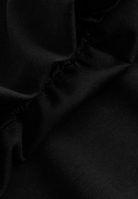 Gros plan d'un tissu noir avec de légers plis et un détail de couture froncée montrant la texture et les coutures.