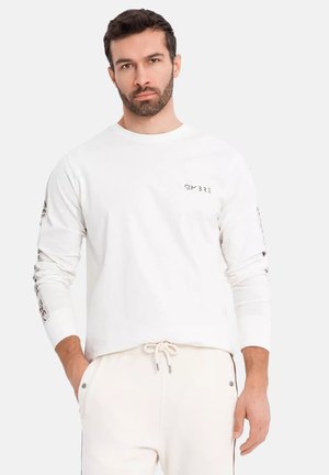White long-sleeve shirt with a round neckline, featuring printed details on sleeves and a small logo on the chest. Soft fabric texture.