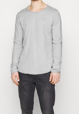 Grijze long-sleeve top van zachte stof, met een ronde halslijn en een licht gebogen zoom. Minimalistisch ontwerp met subtiele branding.