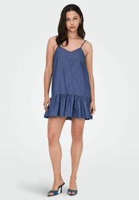 Niebieska sukienka bez rękawów z rozszerzanym dołem w falbanę, z białym wzorem w kropki i cienkimi ramiączkami. Miękka struktura materiału.