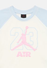 Βαμβακερό μπλουζάκι με ανοιχτό μπλε raglan μανίκια, λευκό σώμα, με ροζ λογότυπο "Air" και γραφικό με φιγούρα που πηδάει πάνω από τον αριθμό "23".