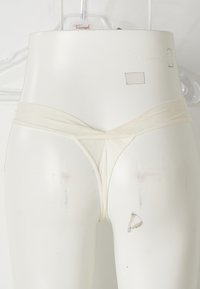 Witte string ondergoed te zien op een mannequin. Heeft een gladde textuur, een V-vormig voorkantontwerp en smalle bandjes.