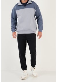 Sudadera gris claro y azul oscuro con cuello de media cremallera, textura suave; combinada con pantalones negros y zapatillas blancas.