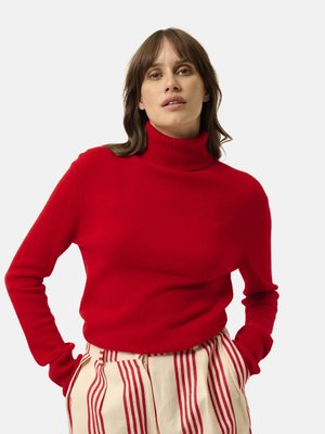 Maglione a dolcevita rosso in morbida lana con polsini a coste, abbinato a pantaloni a righe color crema con linee verticali rosse.
