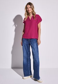 Top fucsia a maniche corte con scollatura a V, abbinato a jeans blu a gamba larga. Tessuto casual e testurizzato, con cuciture visibili e una vestibilità rilassata.