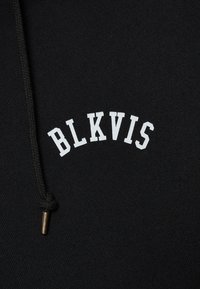 Sweat à capuche noir avec un design de texte blanc incurvé "BLKVIS". Comprend un cordon texturé avec une pointe en métal doré. Texture de tissu douce.