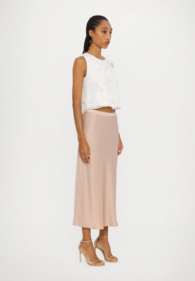 Weißes, floral besticktes Crop-Top mit rundem Halsausschnitt, kombiniert mit einem rosa A-Linien-Midikleid und hautfarbenen High-Heels.