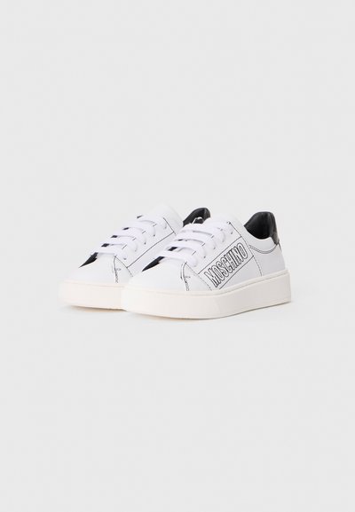 Vita låga sneakers med svarta sömmar, svart hälaccent och "MOSCHINO" branding på sidan, visade på en enkel vit bakgrund.