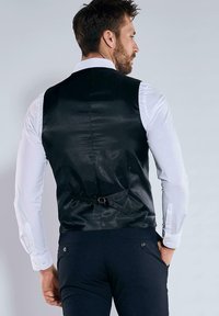 Schwarze Satinveste mit tailliertem Schnitt, mit einer Schnallenverstellung auf der Rückseite, über einem weißen Hemd getragen.