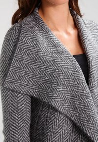 Gray herringbone shawl with a soft texture, featuring wide, folded collar and open front design, shown on a dark top.