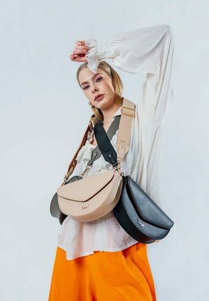 Tři tašky vystavené: béžová zakřivená taška, tmavě šedá taška a černá taška. Všechny mají hladkou kůži, stylová zapínání a nastavitelné popruhy.