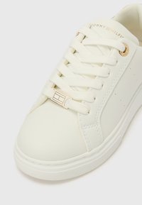 Biały sneaker wykonany z gładkiego materiału syntetycznego, z zaokrąglonym noskiem, zapinany na sznurowadła, z akcentami ze złotych dodatków i subtelnym logo.