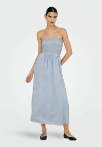 Gestreepte maxi-jurk in blauw en wit, met een gesmokt lijfje, dunne banden en een vloeiende rok. Gemaakt van lichte stof. Platte zwarte schoenen.