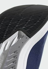 Suola della scarpa in gomma nera testurizzata con grip, intersuola bianca e tomaia in mesh blu, con design curvi distintivi e dettagli di ventilazione.