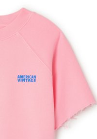 Sweat-shirt rose avec un col rond et des manches raglan. Dispose d'ourlets à franges et d'un logo bleu "AMERICAN VINTAGE" sur la poitrine.