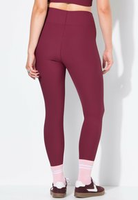 Bordowe legginsy z prążkowanej tkaniny, wysoki stan, dopasowany krój, w połączeniu z różowymi skarpetkami w paski i trampkami.