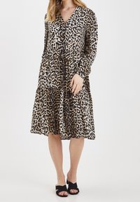 Leopardmönstrad klänning med djup V-ringning, långa ärmar, lager-på-lager kjol och fickor, tillverkad av ett lätt och mjukt tyg.