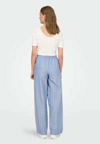 helelillad laiad püksid, millel on vertikaalsed valged triibud, elastse vöökoha ja pehme kangaga. Kandetud koos valge lühikese varrukaga toppiga.