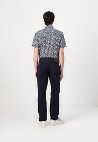 Camicetta a maniche corte di colore blu navy con motivo foglia bianco, abbinata a jeans blu scuro e sneakers bianche, vista da dietro.