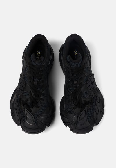 Scarpe sportive nere con tomaia testurizzata, sovrapposizioni in rete e materiale sintetico, sistema di allacciatura prominente e suola in gomma robusta.