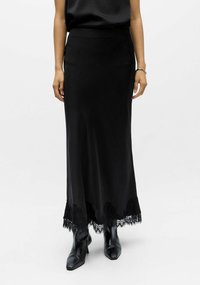 Jupe maxi en satin noir avec une ceinture ajustée et un détail en dentelle délicate à l'ourlet, accompagnée de bottines noires fines à la cheville.