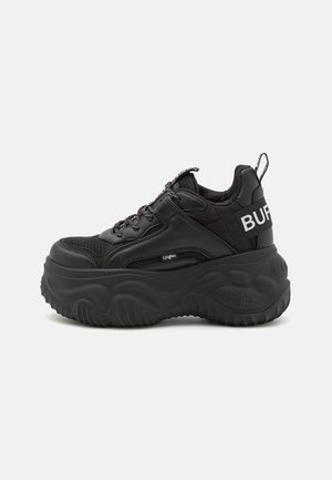 Klotzige schwarze Sneakers mit einem Obermaterial aus Mesh und Leder, dicker Gummisohle und auffälligem Branding an der Seite. Mit Schnürsenkeln und einer Schlaufe zum Hineinschlüpfen.