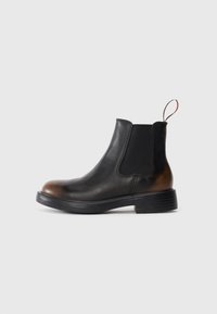 Bottines Chelsea en cuir noir avec bout et talon marron, panneau latéral élastique, languette, et semelle basse empilée sur fond blanc.