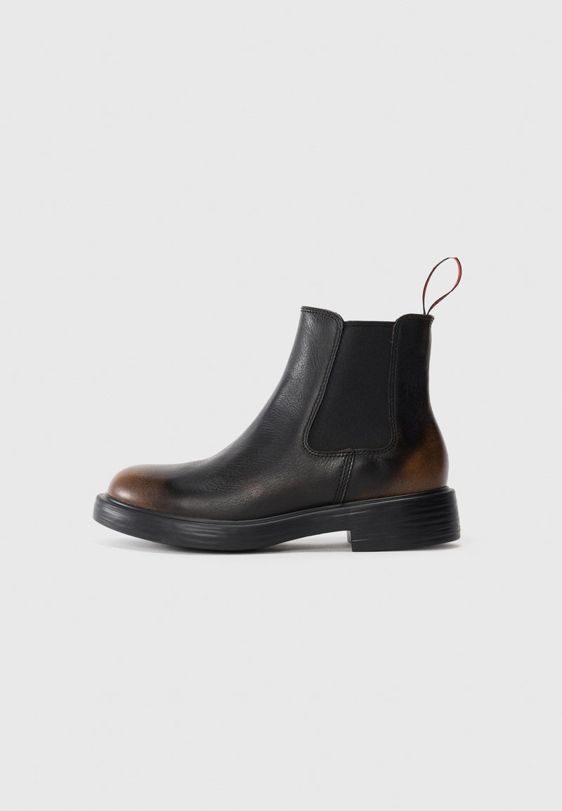 Bottines Chelsea en cuir noir avec bout et talon marron, panneau latéral élastique, languette, et semelle basse empilée sur fond blanc.