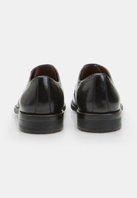 Scarpe di pelle nera con finitura lucida, punta tonda, tacco basso e dettagli cuciti sulla tomaia. Superficie liscia, design classico.