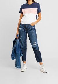 Navy ja roosa värvi lühikeste varrukatega T-särk "TOMMY JEANS" logoga, koos kulunud siniste teksade ja valgete tossudega, hoides nahktagi.