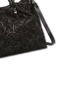 Sac à main en cuir noir avec des motifs en relief en forme de tourbillon circulaire, une fine bandoulière et un petit charm en forme de drapeau italien attaché près de la fermeture éclair.