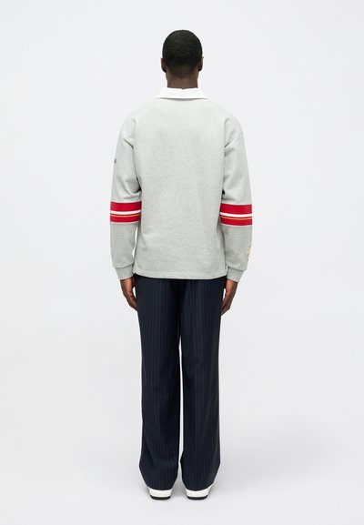 Γκρι φούτερ με κόκκινες και λευκές ρίγες στα μανίκια, άνετη εφαρμογή, λεπτομέρεια στον γιακά, συνδυασμένο με ναυτικά παντελόνια με ρίγες και λευκά αθλητικά παπούτσια.