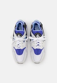 Une paire de Nike Air Huarache blanches, bleues et noires avec des lacets blancs, vue de dessus sur un fond blanc.