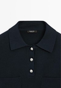 Polo blu navy con un design a maglia testurizzata, dotato di un colletto classico e tre bottoni metallici, e una tasca sul petto.