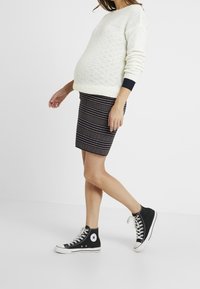 Biała swetrowa bluzka z rypsowymi granatowymi akcentami, dopasowana spódnica w paski w ciemnych odcieniach oraz czarne trampki za kostkę z białą podeszwą.