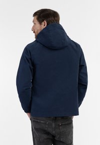 Navy blue hooded jacket with a smooth texture, elastic cuffs, and a relaxed fit. The back features a simple design and no visible accents.