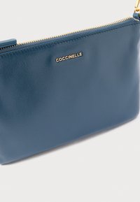 Modrý kožený psaníčko s hladkou texturou, zlatým zipem a viditelným logem značky. Kompaktní design vhodný pro nezbytnosti.