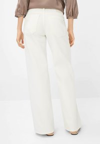 Jean large blanc à taille mi-haute, avec deux poches arrière et une texture subtile. Les détails de couture et l'ourlet net mettent en valeur le design.