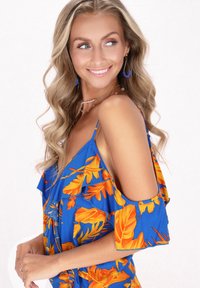 Abito floreale blu con motivi di foglie arancioni, spalle arricciate e tagliato a freddo sulle spalle. Modella accessorize con collane a strati e orecchini.